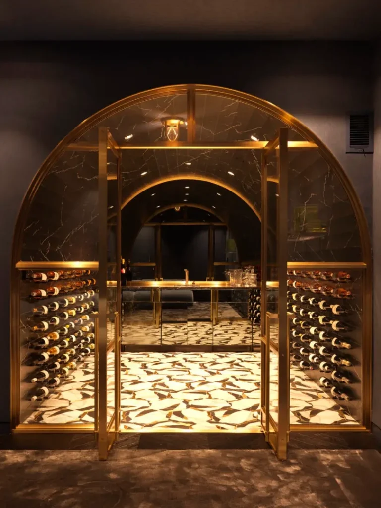 Arched brass framed glass doors to a barrel-vaulted wine cellar with marble and brass inlay flooring